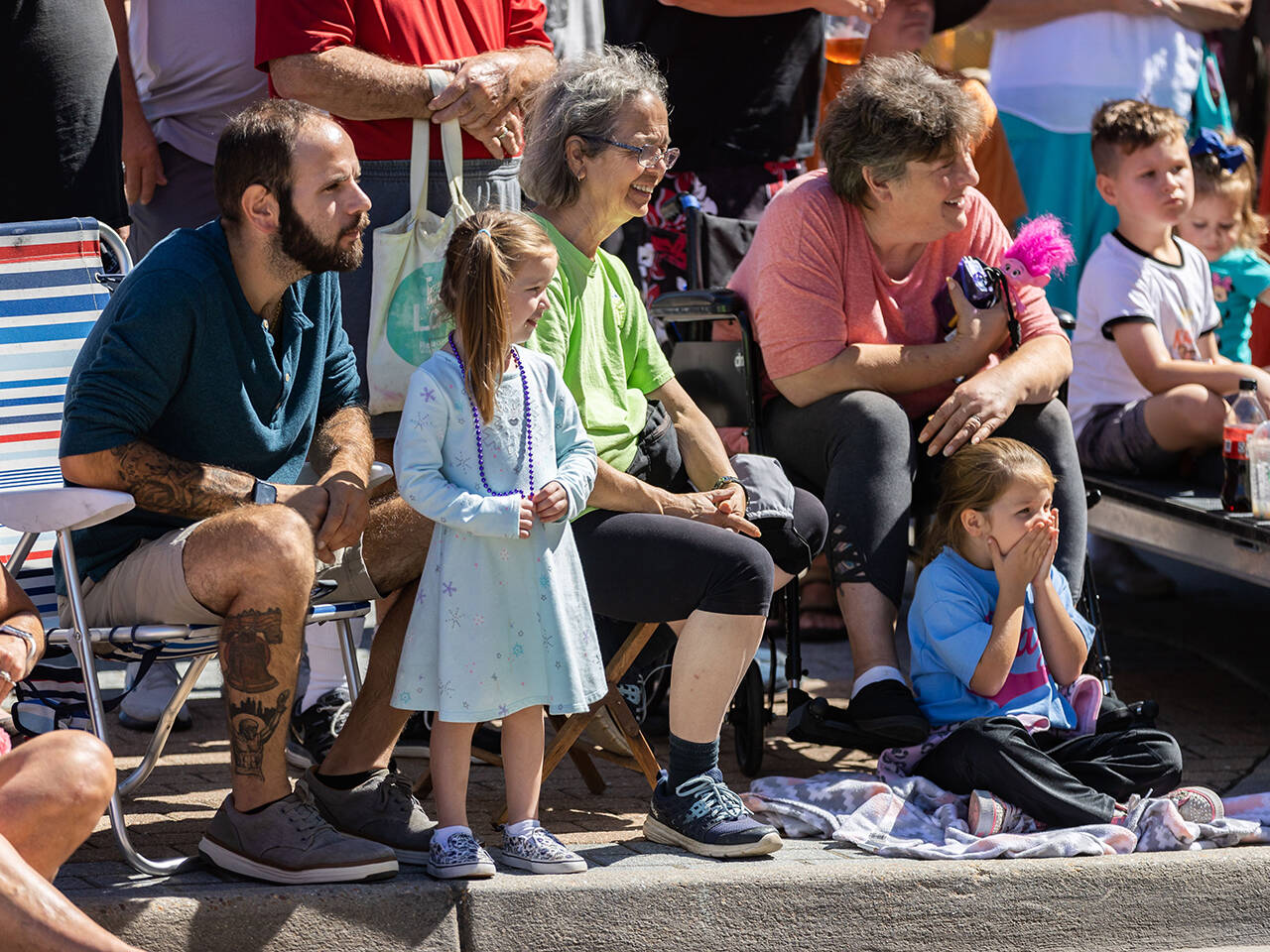 Young girl watching Neptune Festival Grand Parade from curb with family