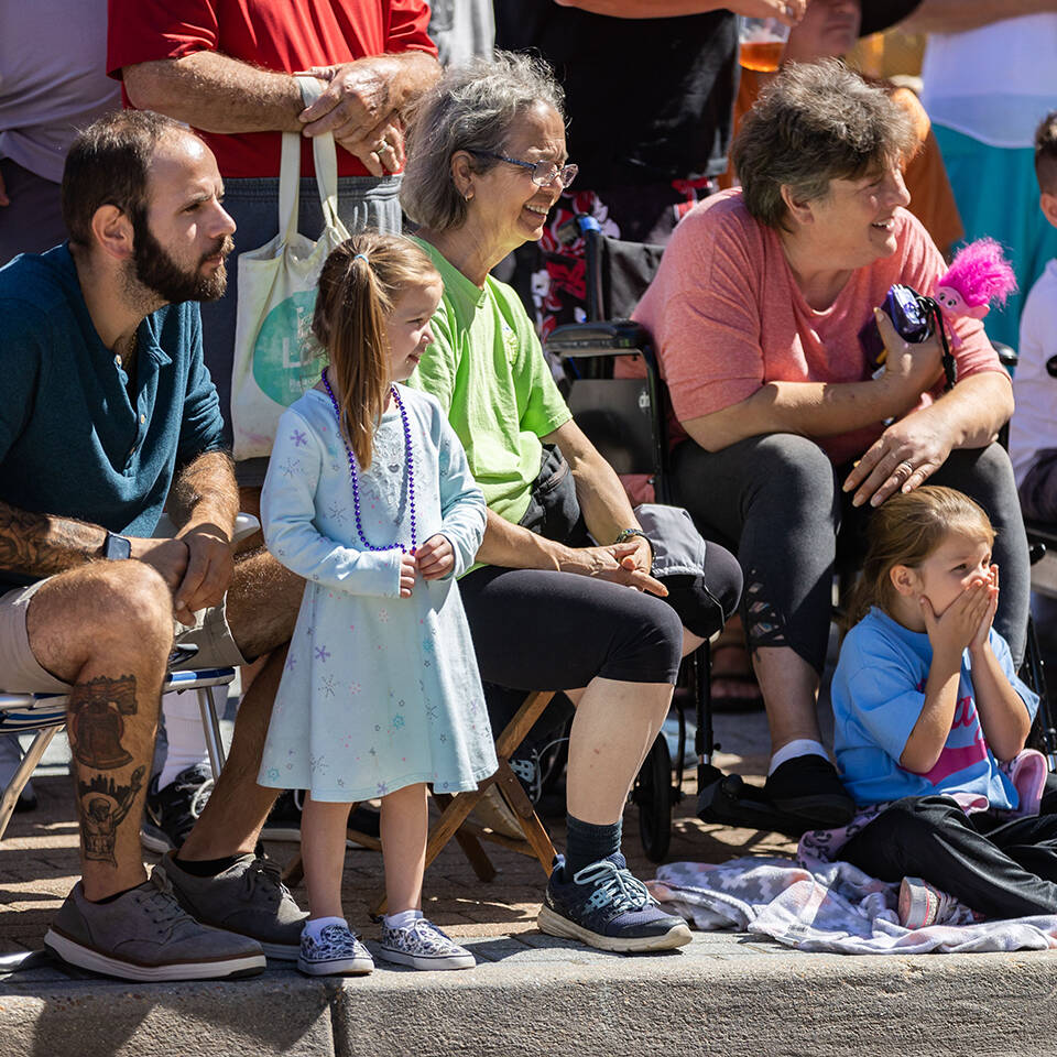 Young girl watching Neptune Festival Grand Parade from curb with family