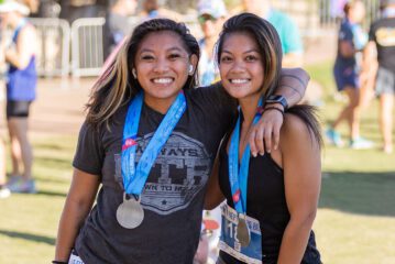 Two young women with arms around each other wearing medals after Neptune's 8K Race