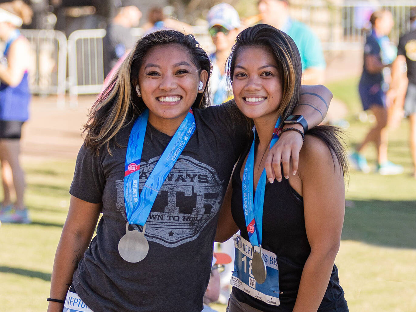 Two young women with arms around each other wearing medals after Neptune's 8K Race