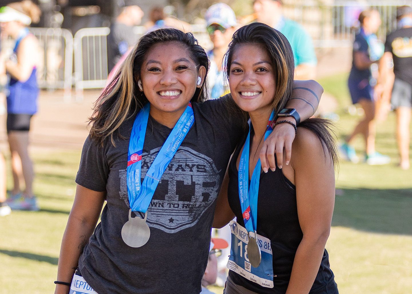 Two young women with arms around each other wearing medals after Neptune's 8K Race